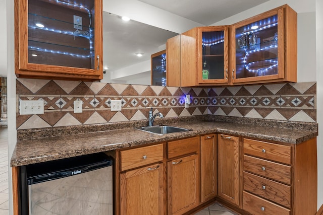 kitchen featuring a sink, tasteful backsplash, dark countertops, and glass insert cabinets