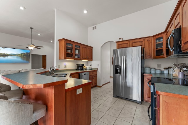 kitchen with a peninsula, glass insert cabinets, a breakfast bar area, a sink, and appliances with stainless steel finishes