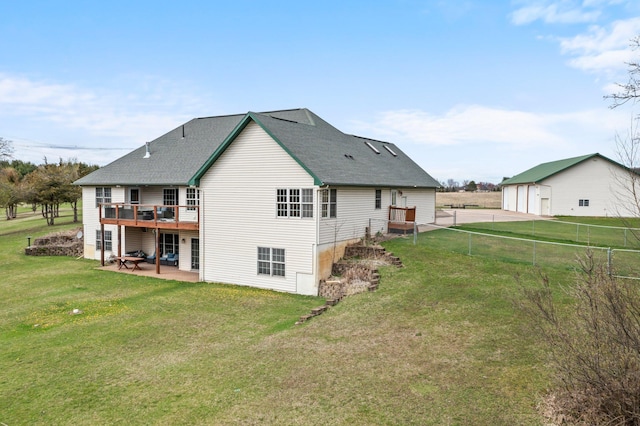 rear view of property with a lawn, a wooden deck, a detached garage, a patio, and a shingled roof
