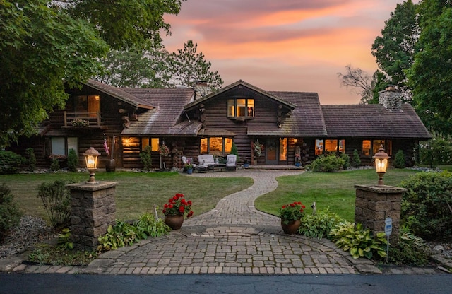 log-style house featuring an outdoor living space, a chimney, a front yard, log siding, and curved driveway