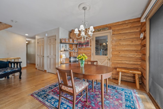 dining area featuring an inviting chandelier, light wood-style flooring, and rustic walls