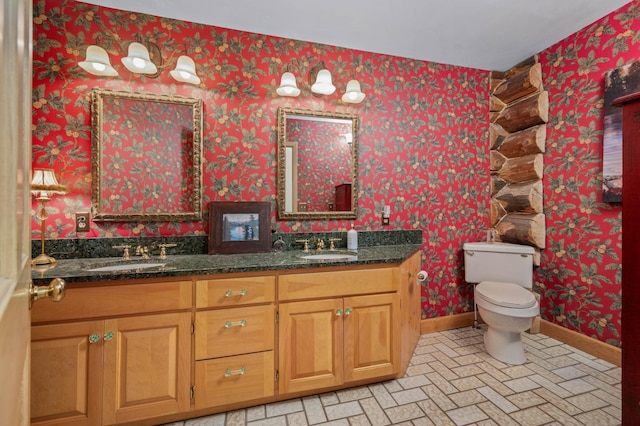 bathroom with a sink, baseboards, toilet, and wallpapered walls