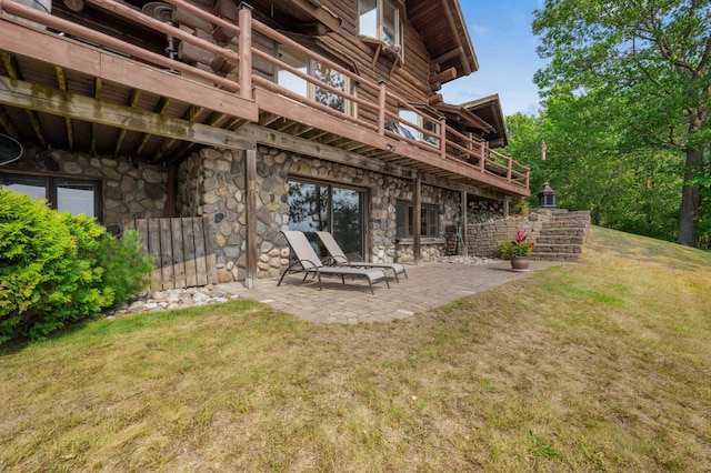 back of house with a balcony, a patio, a yard, and stone siding