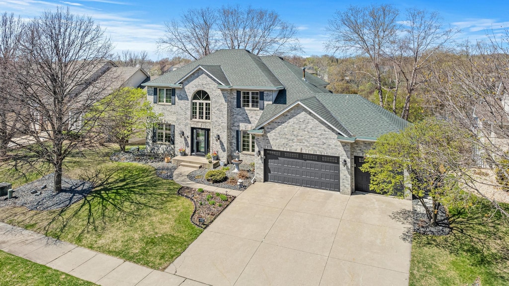 view of front of home featuring a garage, driveway, roof with shingles, a front lawn, and brick siding