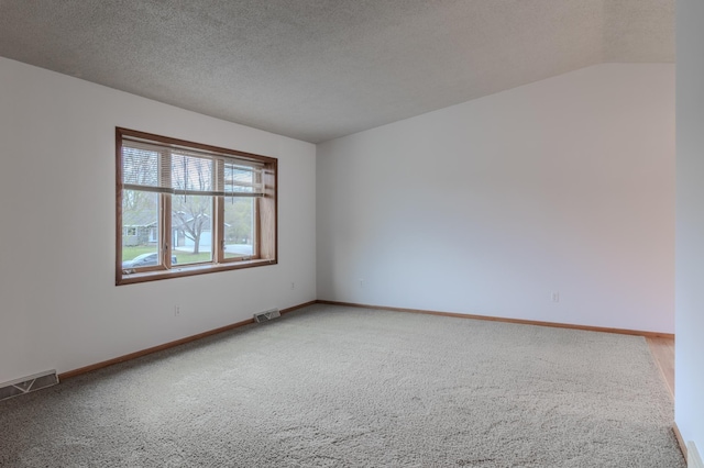 spare room featuring baseboards, light carpet, a textured ceiling, and visible vents