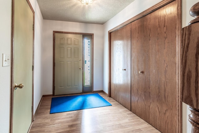 entryway with light wood-type flooring, a textured ceiling, and baseboards