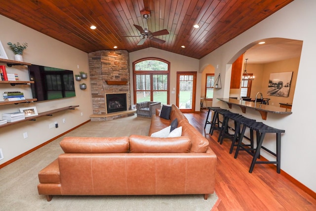 living room featuring a fireplace, arched walkways, ceiling fan with notable chandelier, vaulted ceiling, and wood ceiling
