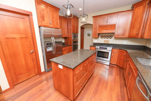 kitchen with brown cabinets, appliances with stainless steel finishes, light wood-style flooring, and custom range hood