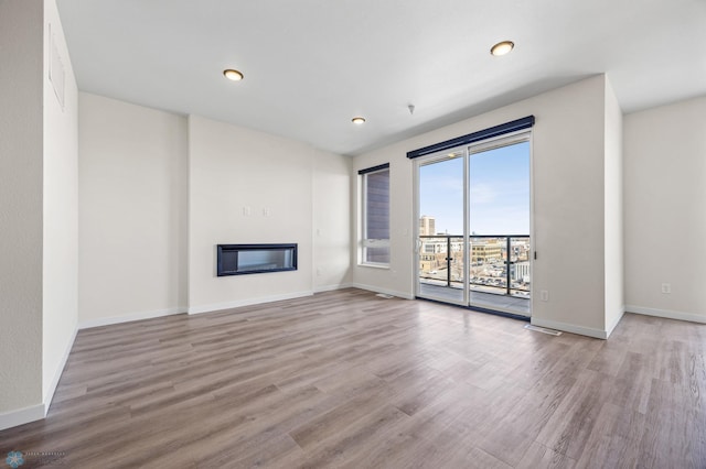 unfurnished living room featuring a glass covered fireplace, baseboards, recessed lighting, and wood finished floors
