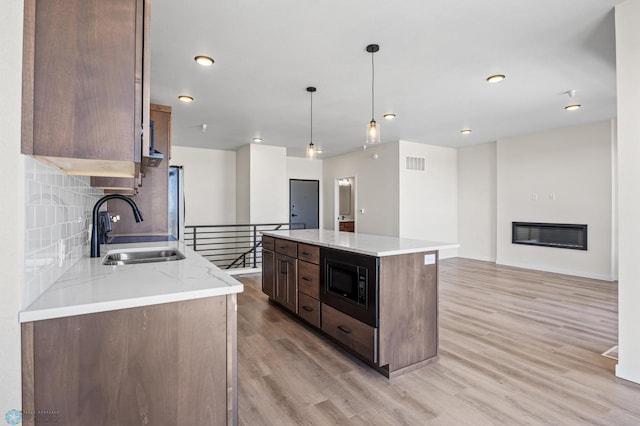 kitchen with visible vents, built in microwave, a sink, light wood finished floors, and a glass covered fireplace