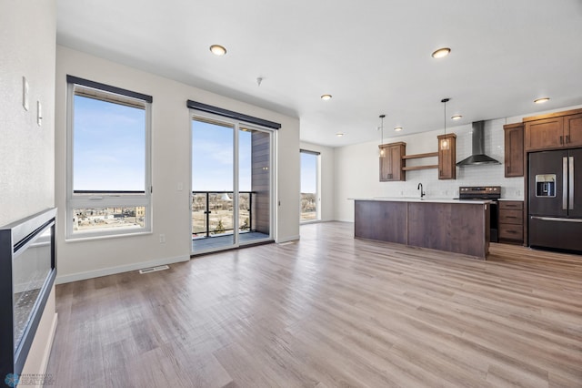 kitchen featuring wall chimney range hood, stainless steel electric range oven, a sink, light wood finished floors, and refrigerator with ice dispenser