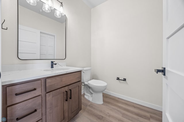 half bath with vanity, baseboards, toilet, and wood finished floors