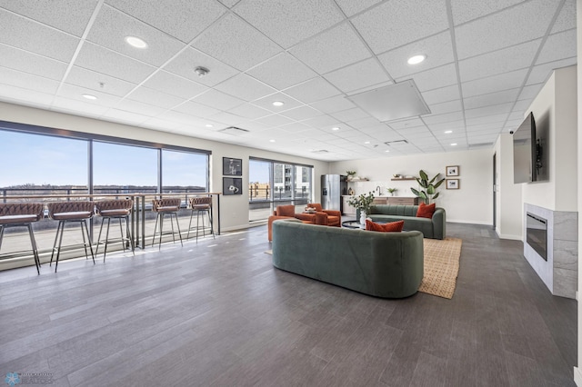 living room featuring baseboards, dark wood finished floors, a glass covered fireplace, and a drop ceiling