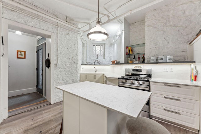 kitchen with light stone counters, gas stove, white cabinetry, wood finished floors, and a kitchen island