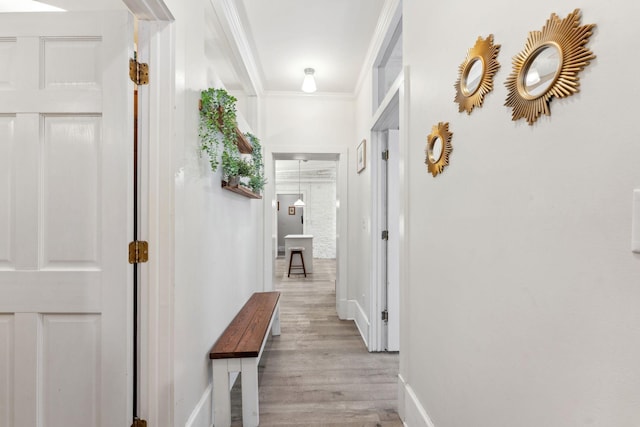 hallway with light wood-style floors, baseboards, and crown molding