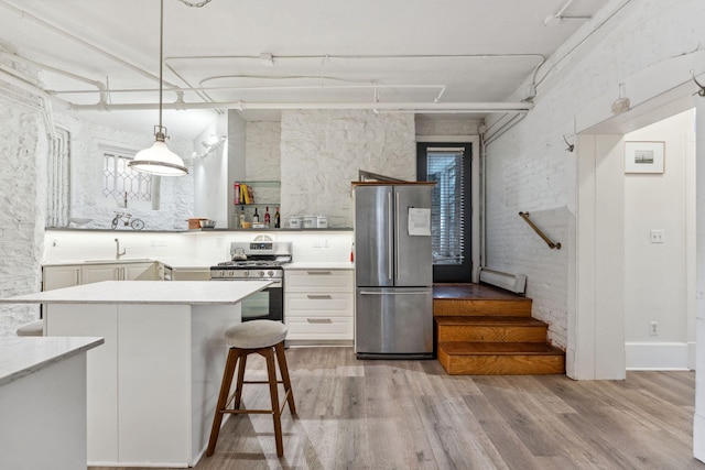 kitchen featuring open shelves, a sink, stainless steel appliances, decorative light fixtures, and wood finished floors