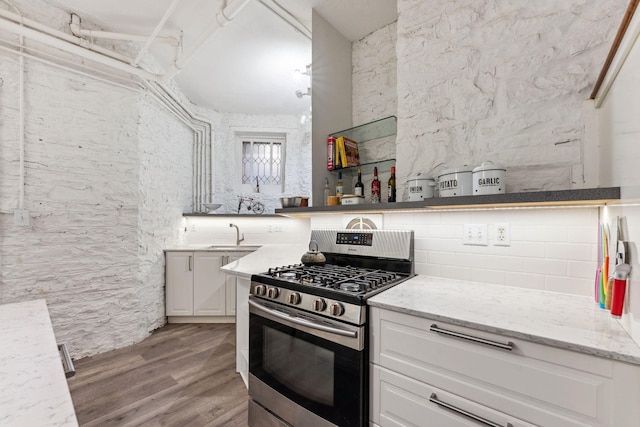 kitchen with light stone counters, light wood-style flooring, white cabinetry, and stainless steel gas stove