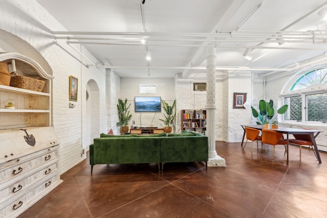 sitting room with concrete flooring, brick wall, decorative columns, and rail lighting