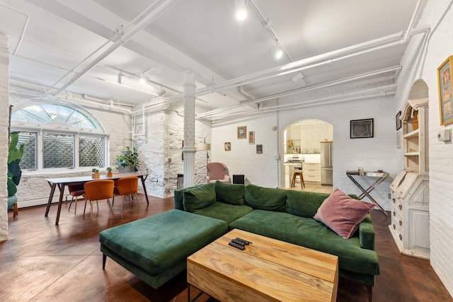 living area featuring arched walkways, baseboard heating, rail lighting, and finished concrete floors