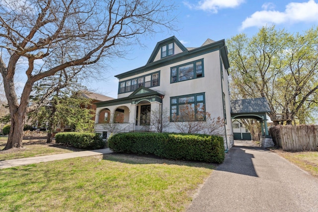 view of front facade featuring a front lawn, fence, stucco siding, driveway, and a carport