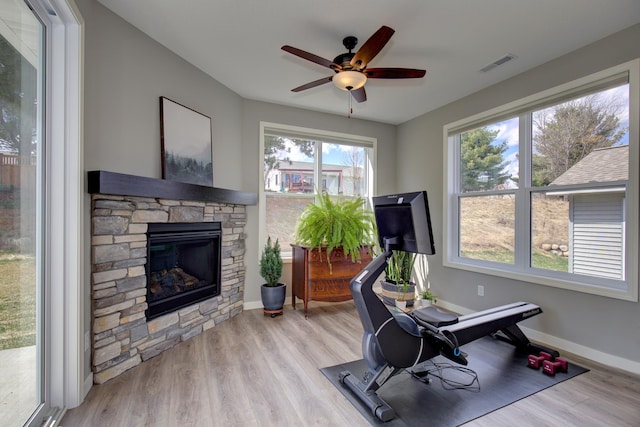 workout area featuring ceiling fan, visible vents, a fireplace, baseboards, and light wood-style floors