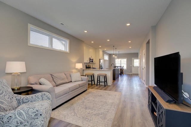 living area with visible vents, an inviting chandelier, baseboards, recessed lighting, and light wood-style flooring