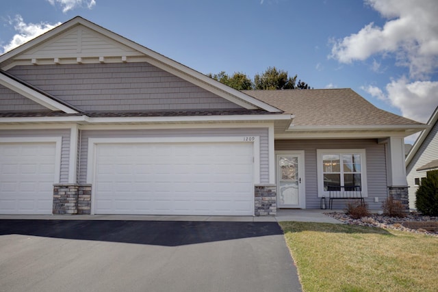 craftsman-style home featuring an attached garage, aphalt driveway, and stone siding