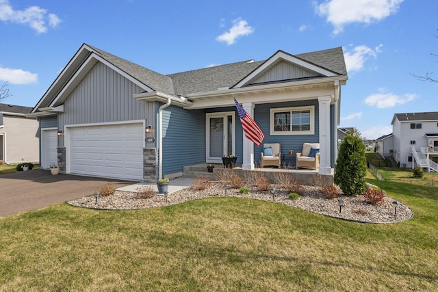 view of front facade with a front lawn, aphalt driveway, a garage, board and batten siding, and covered porch