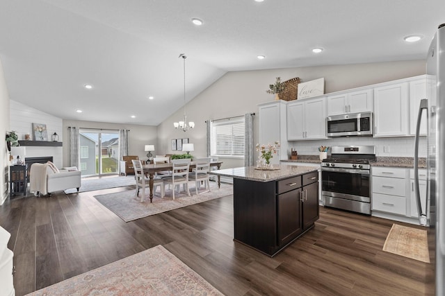 kitchen with open floor plan, dark wood-style floors, white cabinetry, light stone counters, and appliances with stainless steel finishes