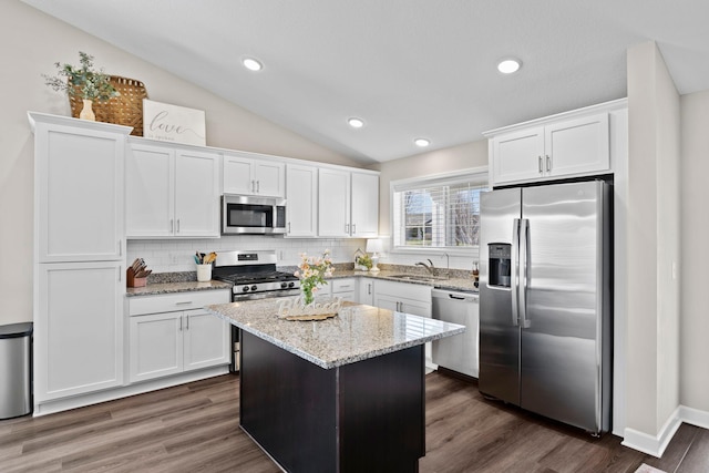kitchen featuring white cabinets, appliances with stainless steel finishes, a sink, backsplash, and vaulted ceiling