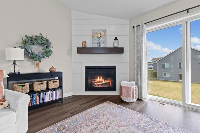 living area with visible vents, a large fireplace, wood finished floors, and lofted ceiling