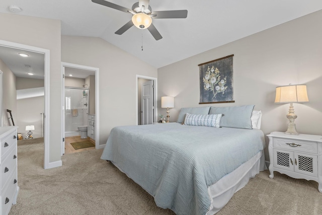 bedroom featuring a ceiling fan, light colored carpet, baseboards, lofted ceiling, and ensuite bath