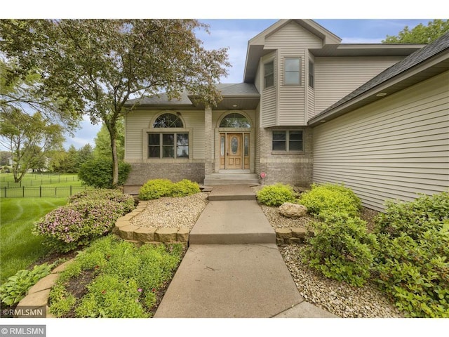 doorway to property featuring a yard, brick siding, fence, and a shingled roof