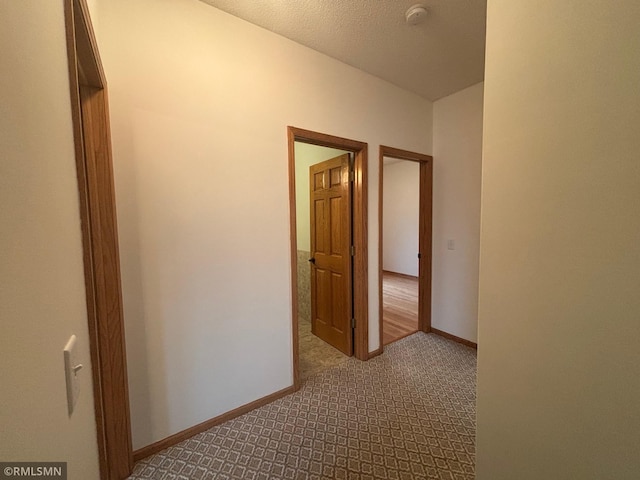 hallway featuring dark carpet and baseboards