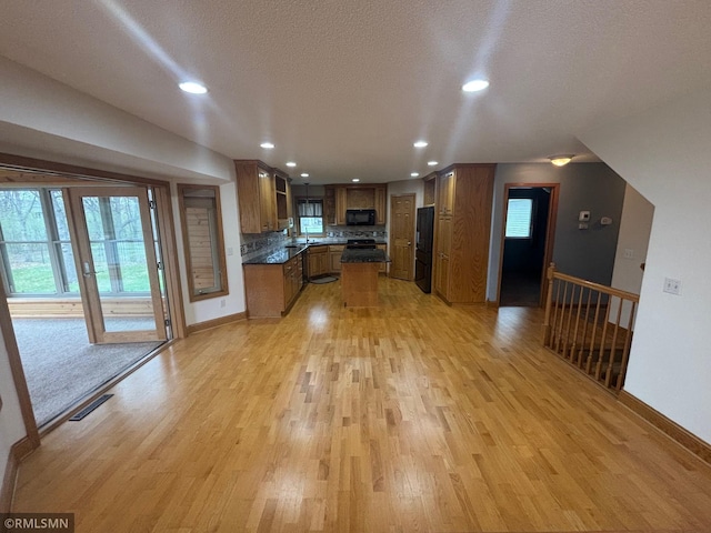 kitchen with brown cabinets, black microwave, light wood finished floors, baseboards, and refrigerator