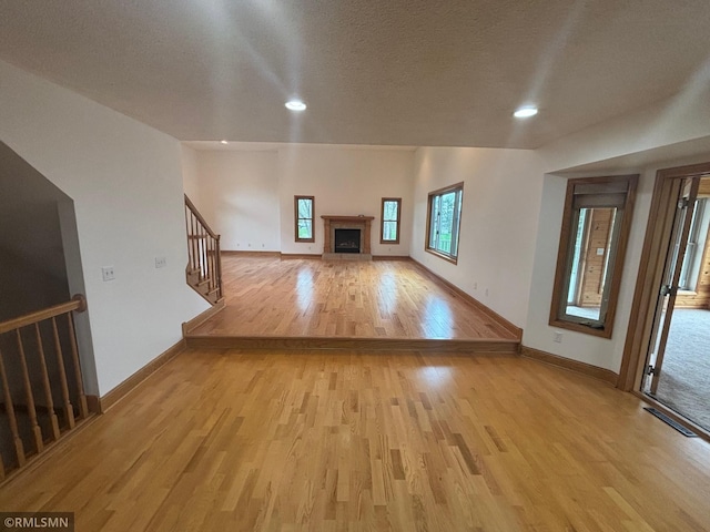 unfurnished living room with stairs, baseboards, light wood-style flooring, and a fireplace