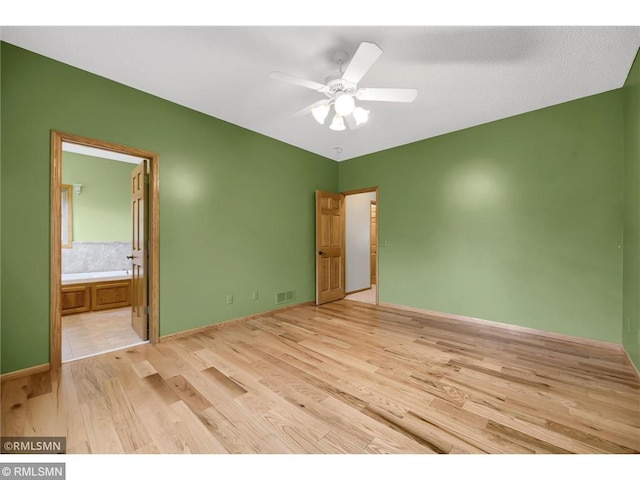 unfurnished bedroom featuring connected bathroom, light wood finished floors, a ceiling fan, baseboards, and visible vents