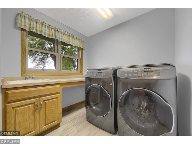 laundry room featuring a textured ceiling, washing machine and clothes dryer, a sink, cabinet space, and light wood finished floors