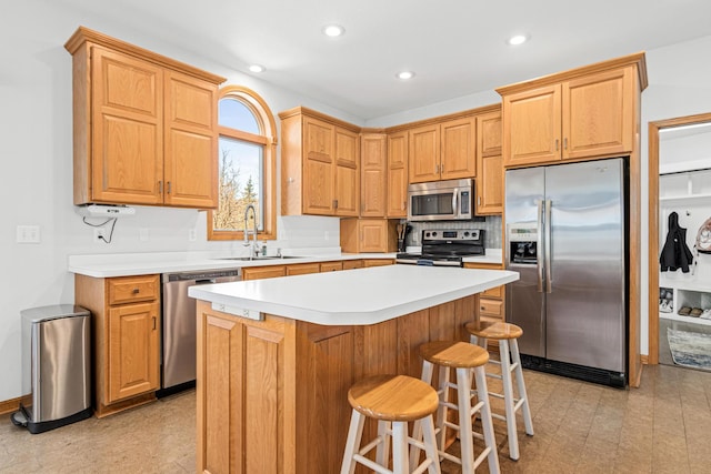kitchen featuring appliances with stainless steel finishes, a center island, a sink, light countertops, and a breakfast bar