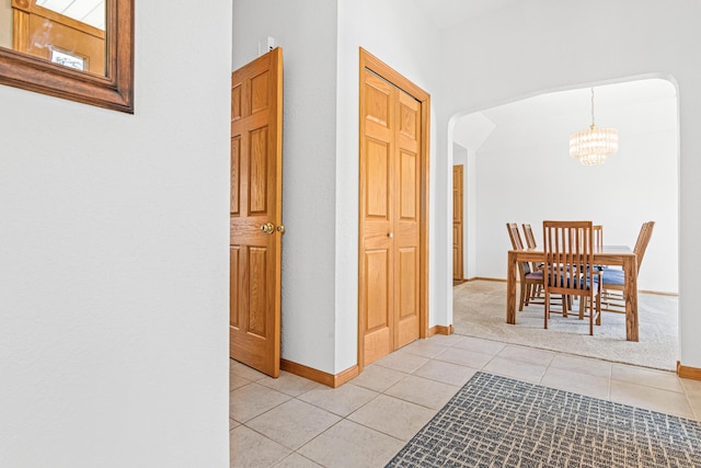 hall featuring light tile patterned floors, baseboards, and a chandelier