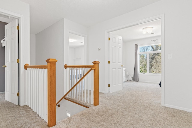 corridor featuring carpet floors, baseboards, and an upstairs landing