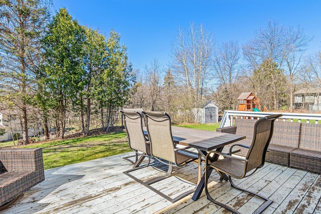 wooden terrace featuring outdoor dining area, an outdoor structure, a playground, a storage unit, and a yard