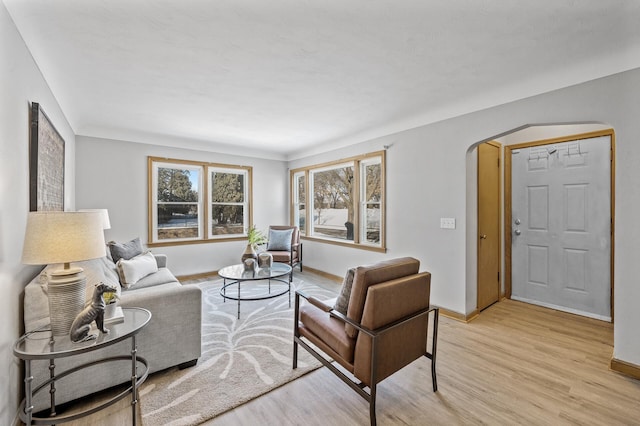 living room with arched walkways, baseboards, and light wood-style flooring