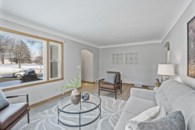 living room with arched walkways, baseboards, visible vents, and wood finished floors