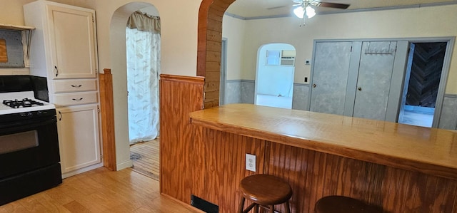 kitchen with a breakfast bar, light wood-type flooring, white cabinetry, range with gas cooktop, and arched walkways