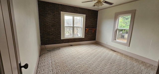 empty room with ceiling fan, brick wall, light colored carpet, crown molding, and baseboards