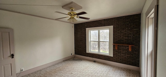 spare room featuring baseboards, a ceiling fan, and brick wall