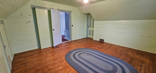 additional living space with visible vents, hardwood / wood-style flooring, wood walls, and vaulted ceiling