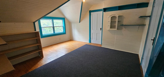 additional living space with wood walls, vaulted ceiling, and hardwood / wood-style flooring