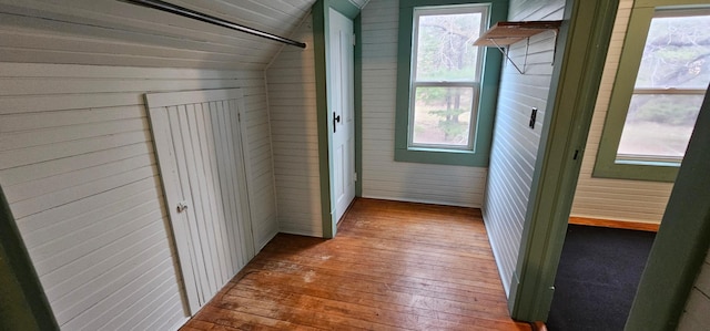 corridor featuring hardwood / wood-style flooring, wood walls, and lofted ceiling